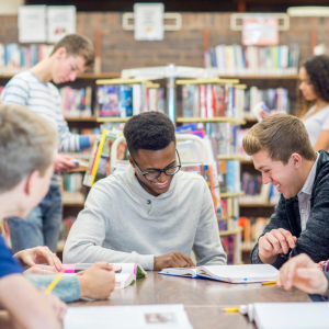 Teens looking at books at a desk in a library